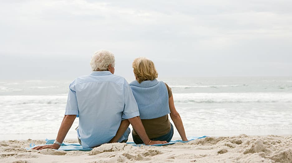 Senior couple sitting on the beach after selling their life insurance policy