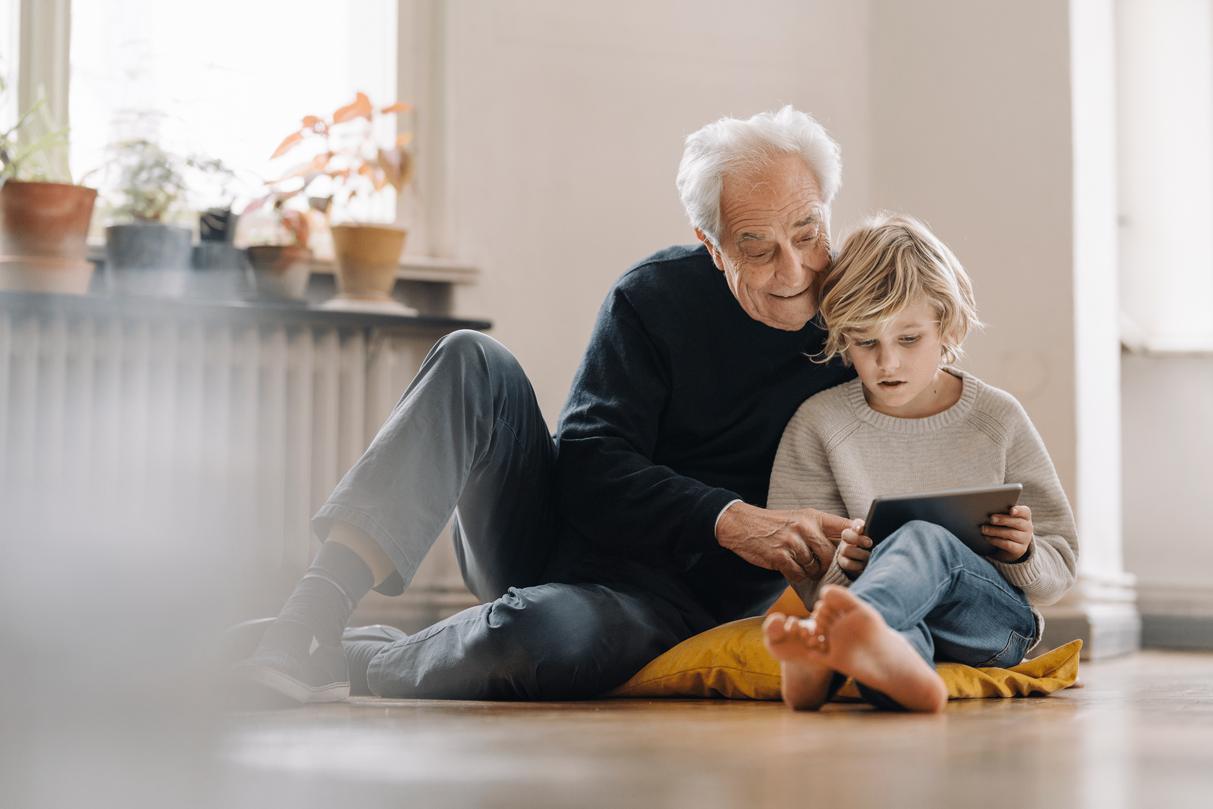 A grandfather sitting on the floor reading with his grandchild